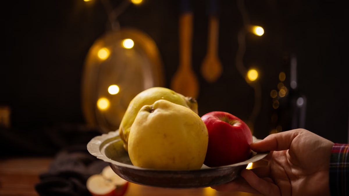 A rustic composition featuring apples and quince illuminated by warm fairy lights indoors.